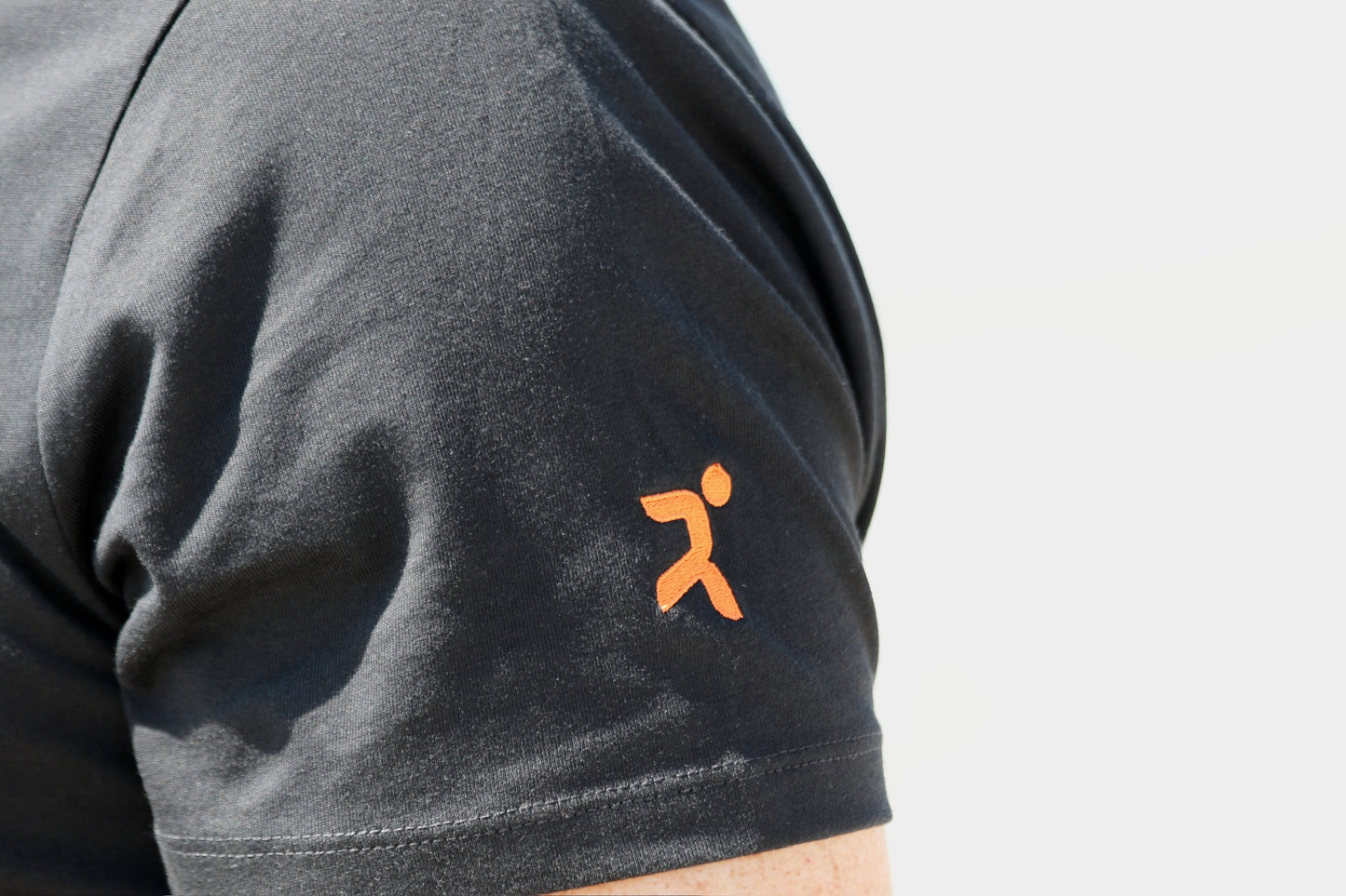 detalle ampliado de la manga corta izquierda con el logo de h&j en color naranja sobre negro con fondo de mar difuminado