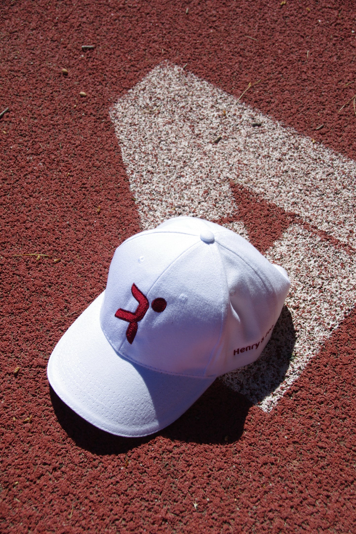 Gorra blanca Henry and John con logo rojo magenta central sobre pista de atletismo