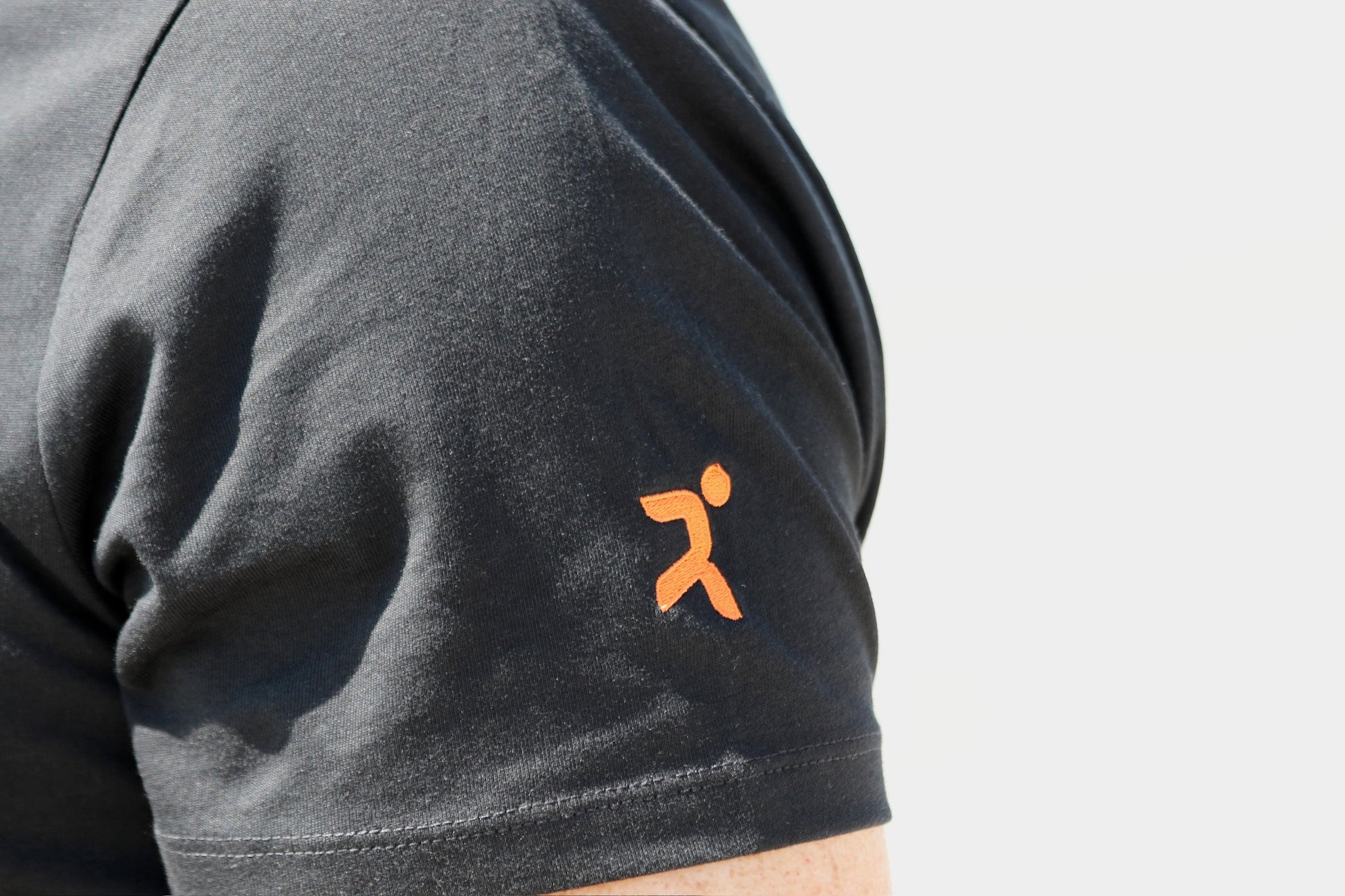detalle ampliado de la manga corta izquierda con el logo de h&j  en color naranja sobre negro con fondo de mar difuminado